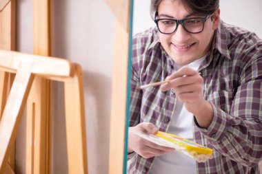 Genç erkek sanatçı parlak stüdyoda resimler çiziyor.