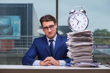 Yığınla evrak işi ve alarm sistemi olan bir iş adamı.