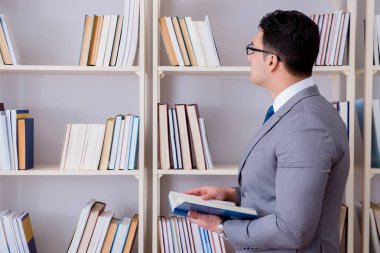 İşadamı öğrenci kütüphanede bir kitap okuyor.