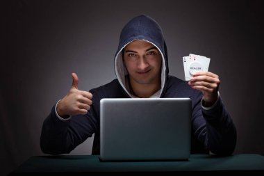 Kapüşonlu genç adam dizüstü bilgisayarın önünde oturuyor.