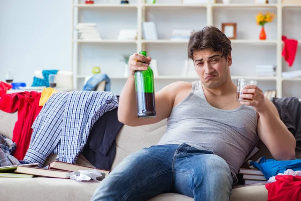 Young man student drunk drinking alcohol in a messy room