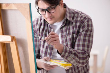 Genç erkek sanatçı parlak stüdyoda resimler çiziyor.