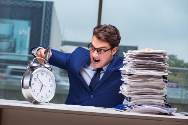 Yığınla evrak işi ve alarm sistemi olan bir iş adamı.