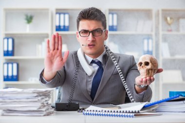 Ofisteki işadamı elinde insan kafatasıyla sigara içiyor.