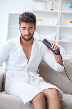 Saç kurutma makinesiyle saç kurutan genç bir adam.