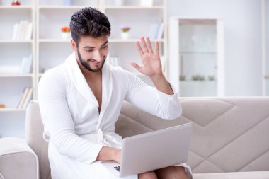 Genç adam evde dizüstü bilgisayarla çalışıyor.