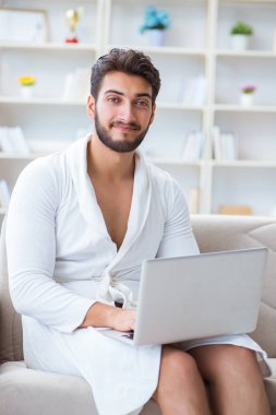 Genç adam evde dizüstü bilgisayarla çalışıyor.