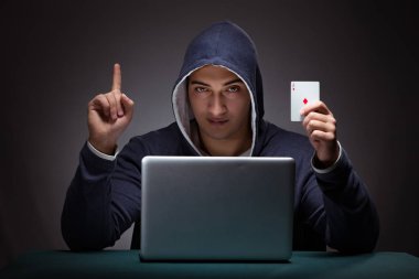 Kapüşonlu genç adam dizüstü bilgisayarın önünde oturuyor.