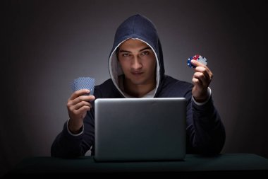 Kapüşonlu genç adam dizüstü bilgisayarın önünde oturuyor.