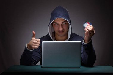 Kapüşonlu genç adam dizüstü bilgisayarın önünde oturuyor.