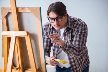 Genç erkek sanatçı parlak stüdyoda resimler çiziyor.