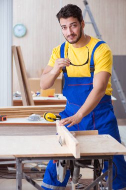 Genç bir marangoz dairesel testereyle odun kesiyor.