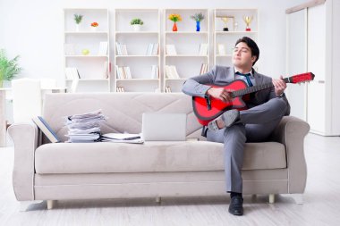 Evde gitar çalan bir iş adamı.