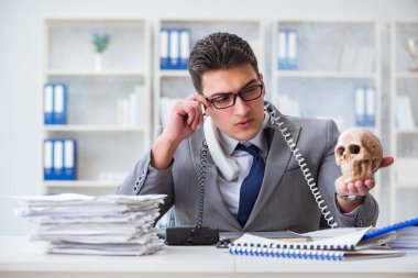 Ofisteki işadamı elinde insan kafatasıyla sigara içiyor.