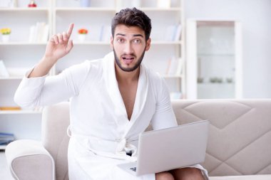 Genç adam evde dizüstü bilgisayarla çalışıyor.