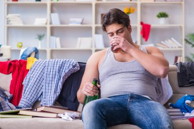 Dağınık bir odada alkol alan genç bir öğrenci.