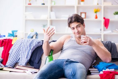 Dağınık bir odada alkol alan genç bir öğrenci.