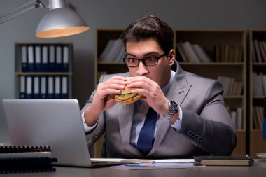 Gece geç saatte iş adamı hamburger yiyor.