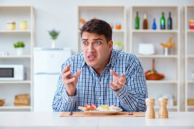 Genç koca öğle yemeğinde tatsız yemekler yiyor.