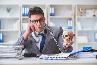 Ofisteki işadamı elinde insan kafatasıyla sigara içiyor.