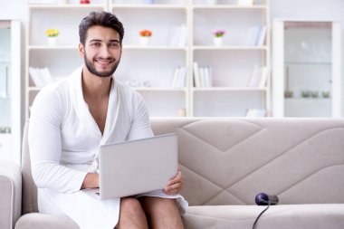 Genç adam evde dizüstü bilgisayarla çalışıyor.