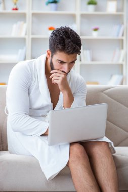 Genç adam evde dizüstü bilgisayarla çalışıyor.