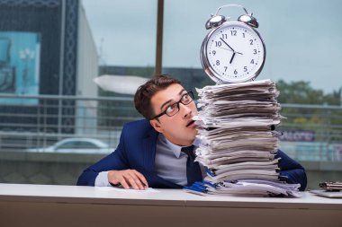 Yığınla evrak işi ve alarm sistemi olan bir iş adamı.