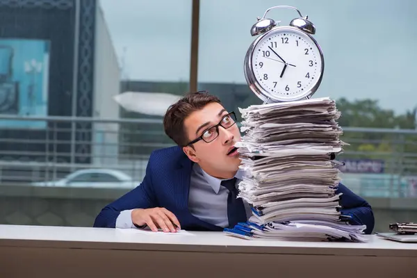 Yığınla evrak işi ve alarm sistemi olan bir iş adamı.