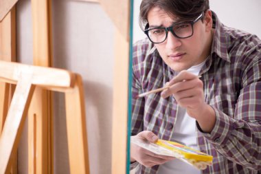 Genç erkek sanatçı parlak stüdyoda resimler çiziyor.