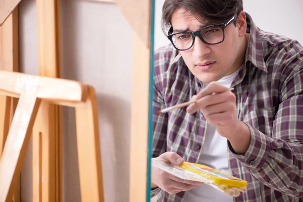 Genç erkek sanatçı parlak stüdyoda resimler çiziyor.