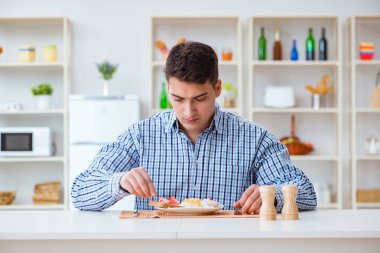 Genç koca öğle yemeğinde tatsız yemekler yiyor.