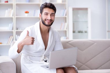 Genç adam evde dizüstü bilgisayarla çalışıyor.