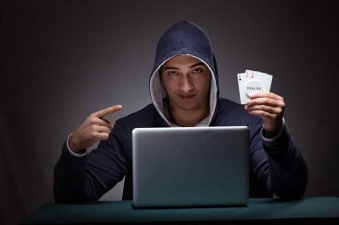 Kapüşonlu genç adam dizüstü bilgisayarın önünde oturuyor.