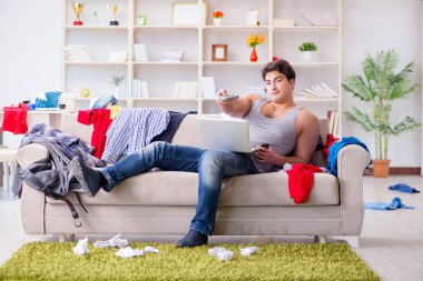 Genç adam dağınık bir odada çalışıyor.