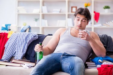 Dağınık bir odada alkol alan genç bir öğrenci.