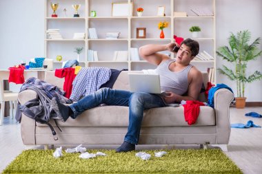 Genç adam dağınık bir odada çalışıyor.