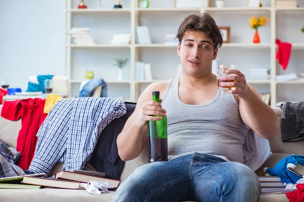 Junger Mann Student betrunken Alkohol trinken in einem chaotischen Zimmer — Stockfoto
