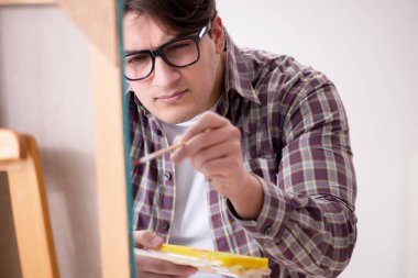 Genç erkek sanatçı parlak stüdyoda resimler çiziyor.