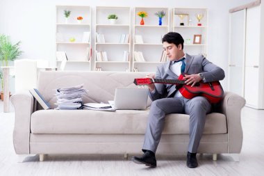 Evde gitar çalan bir iş adamı.