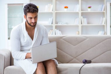 Genç adam evde dizüstü bilgisayarla çalışıyor.