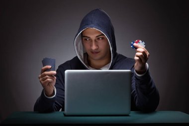 Kapüşonlu genç adam dizüstü bilgisayarın önünde oturuyor.