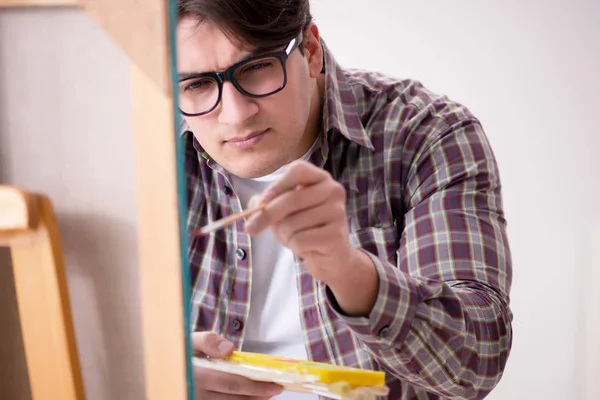 Genç erkek sanatçı parlak stüdyoda resimler çiziyor.