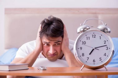 Yataktaki adam alarm yüzünden uykusuzluk çekiyor.