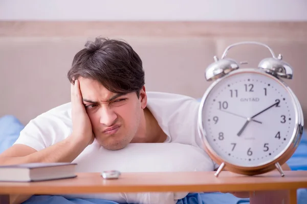 Мужчина в постели расстроен страданием от бессонницы с будильником — стоковое фото