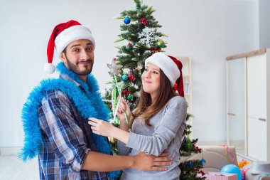 Genç aile Noel ağacını mutlu bir vesileyle süslüyor.