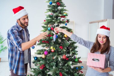 Genç aile Noel ağacını mutlu bir vesileyle süslüyor.