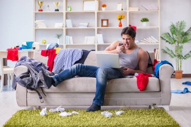 Genç adam dağınık bir odada çalışıyor.