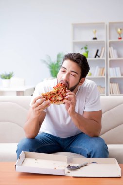 Pizza yiyen adam evde yemek yiyor, dinleniyor.