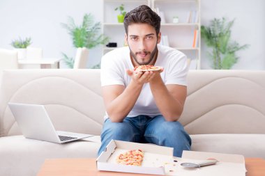 Pizza yiyen adam evde yemek yiyor, dinleniyor.