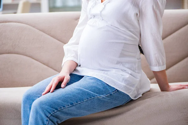 Беременная женщина с животом, сидящая дома на диване — стоковое фото